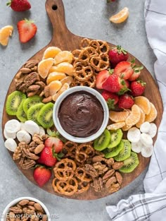 a platter filled with fruit, nuts and chocolate dip surrounded by pretzels