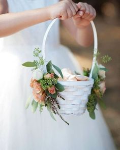 a person holding a white basket with flowers in it and greenery on the handle