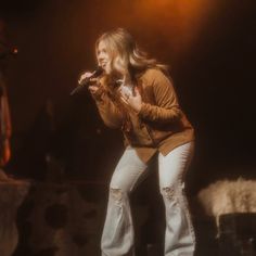 a woman standing on top of a stage holding a microphone in her hand and looking at the ground