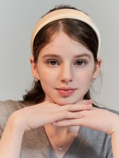 a young woman wearing a white headband with her hands on her chin looking at the camera