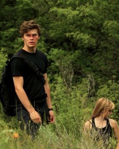 a young man and woman walking through tall grass