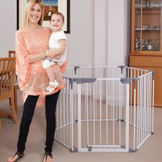 a woman holding a baby in her arms next to a white crib and table