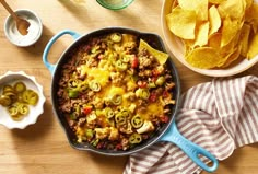 a skillet filled with mexican food next to bowls of tortilla chips and olives