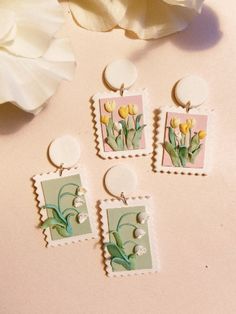 four earrings with flowers on them sitting next to a white flower and a pink background