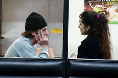 a man sitting next to a woman in front of a window talking on a cell phone