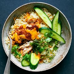 a bowl filled with rice, cucumber and meat on top of it next to a fork