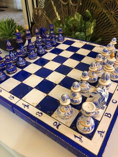 a blue and white chess board with many pieces on it, sitting next to a potted plant