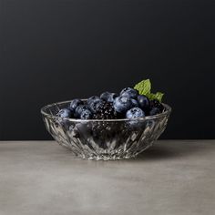 a glass bowl filled with blueberries sitting on top of a gray counter next to a green leaf