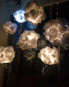 some lights that are hanging from the ceiling in front of a window with clouds on it