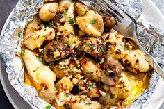 a close up of a plate of food with potatoes and mushrooms on foil wrapped in foil