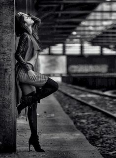 black and white photograph of woman leaning against wall in train station with her legs crossed