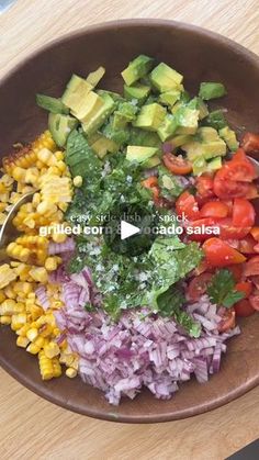 a bowl filled with chopped vegetables and avocado on top of a wooden table