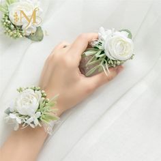 two white roses are being held by someone's hand on a bed with the letter m