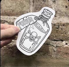 a hand holding up a sticker with a skull in a bottle on the front