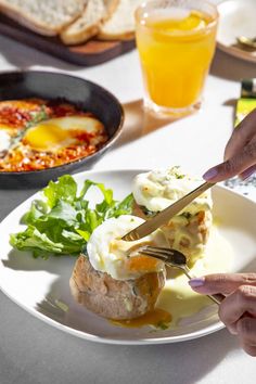 a person cutting into a sandwich on top of a white plate next to other food