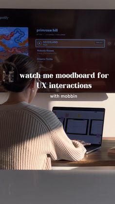 a woman sitting in front of a laptop computer on top of a wooden desk next to a monitor