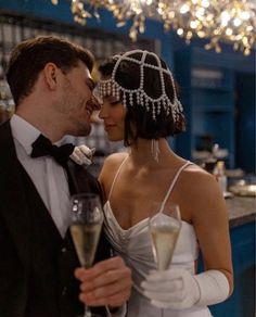 a bride and groom holding champagne flutes in front of a chandelier filled with lights