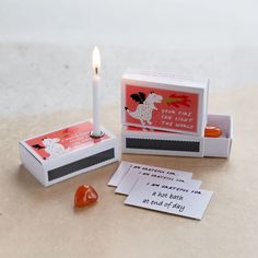 a matchbox with a lit candle next to it and some cards on the table