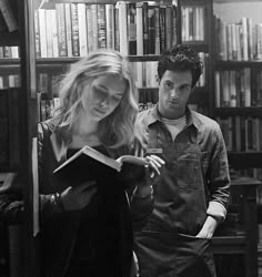 a man standing next to a woman in front of a book shelf filled with books