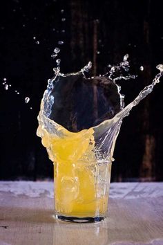 a glass filled with yellow liquid on top of a wooden table next to a black wall