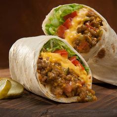 two burritos with meat, cheese and lettuce on a cutting board