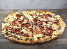 a pizza sitting on top of a wooden table covered in cheese and bacon toppings