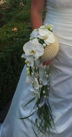 a woman in a wedding dress holding a bouquet of white orchids and greenery