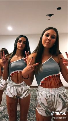 two women in silver and white outfits making the peace sign