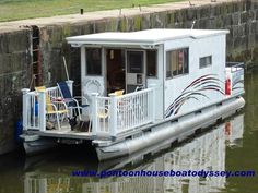 a houseboat is docked at the edge of a canal with chairs on it's deck