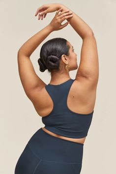 a woman with her arms above her head, wearing a dark blue sports bra top and leggings