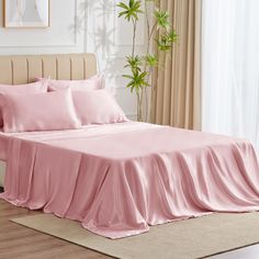 a bed with pink sheets and pillows on top of it in a room next to a potted plant