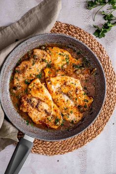 a pan filled with chicken and sauce on top of a woven place mat next to a knife