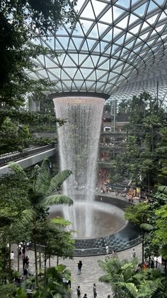 an indoor waterfall in the middle of a building with lots of trees and people walking around