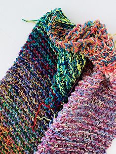 three different colored knitted scarves sitting next to each other on a white surface