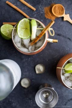 two glasses filled with ice, lime and cinnamon on top of a blue countertop