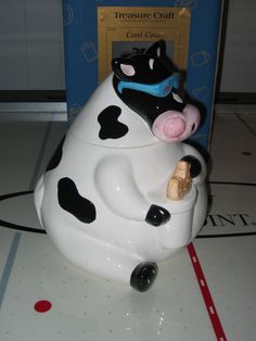 a cow shaped cookie jar sitting on top of a white tile floor next to a blue box