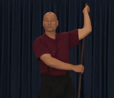 a man holding a stick in front of a blue curtain with his arm extended to the side