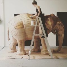 a woman is standing on a ladder next to an elephant made out of wooden planks