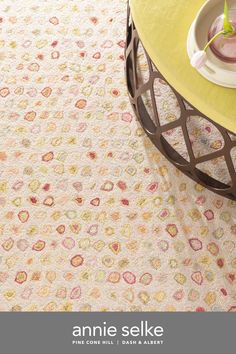 a yellow table with a white plate on top of it next to a flowery rug