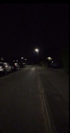 cars are parked on the side of the road at night with street lights in the background