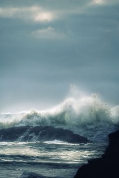 a large wave crashing into the ocean on a cloudy day