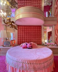 a round bed with pink bedspread and pillows in a room decorated with chandeliers