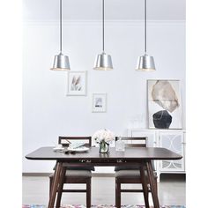 a dining room table with four lights hanging from it's ceiling and an area rug on the floor