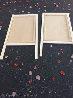 two wooden frames sitting next to each other on a black surface with leaves scattered around them