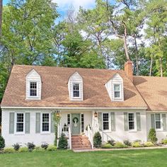 a white house with green shutters on the front and side windows, surrounded by trees