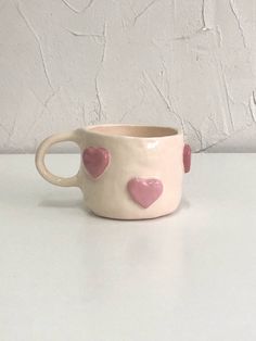 a white cup with pink hearts on the outside and inside is sitting on a table