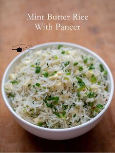 a white bowl filled with rice and green onions on top of a wooden table next to a