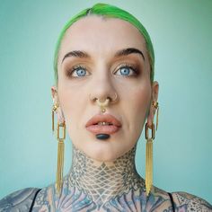 a woman with green hair and piercings on her face is looking at the camera