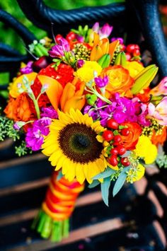 a bridal bouquet with sunflowers, roses and other flowers on a bench