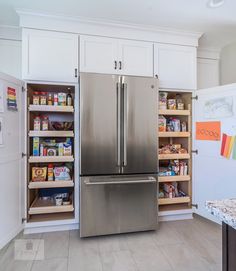 a stainless steel refrigerator in a kitchen with white cupboards and shelves filled with food